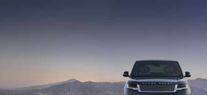 Range Rover eléctrico visto de frente sobre una carretera oscura, con montañas al fondo durante el atardecer.