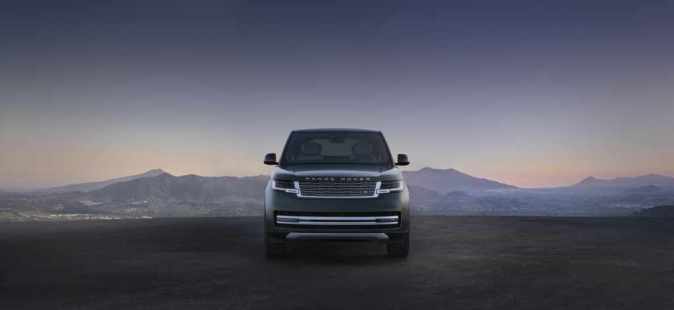 Range Rover eléctrico visto de frente sobre una carretera oscura, con montañas al fondo durante el atardecer.