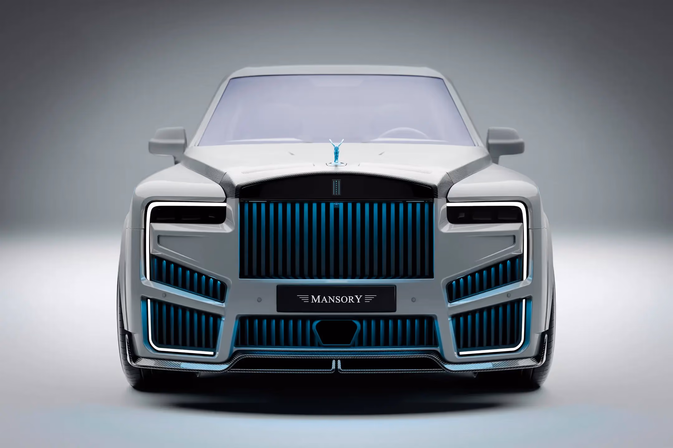 Rolls-Royce Cullinan Mansory blanco visto de frente, con parrilla iluminada en azul, kit aerodinámico y emblema Spirit of Ecstasy.