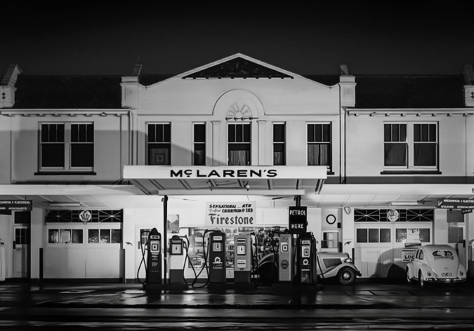 Estación de servicio histórica McLaren’s de noche con bombas de gasolina clásicas y coches vintage.