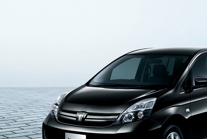 Toyota Isis negro, monovolumen japonés, fotografiado en un estudio sobre una superficie pavimentada.