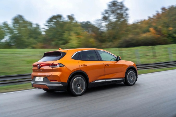 VinFast VF8 naranja en movimiento por carretera, vista trasera dinámica y elegante.