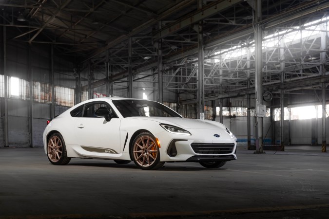 Subaru BRZ blanco de tres cuartos delanteros en nave industrial, faros LED y rines bronce.