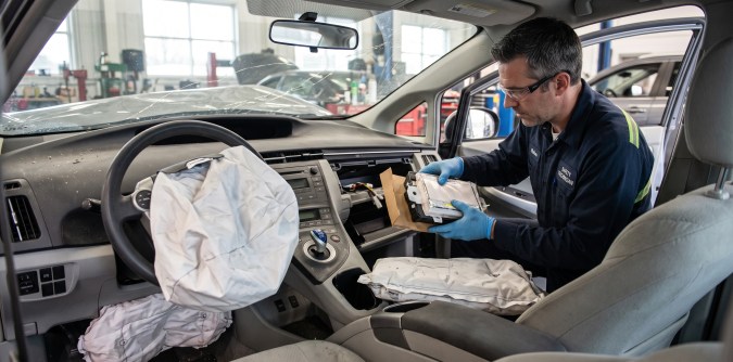 Técnico de seguridad cambiando airbags desplegados en taller de reparación automotriz.