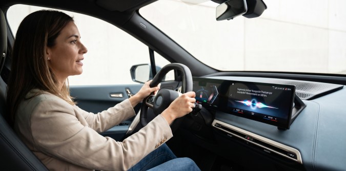 Mujer conduce un automóvil mientras la pantalla multimedia muestra una alerta de navegación premium por suscripción.