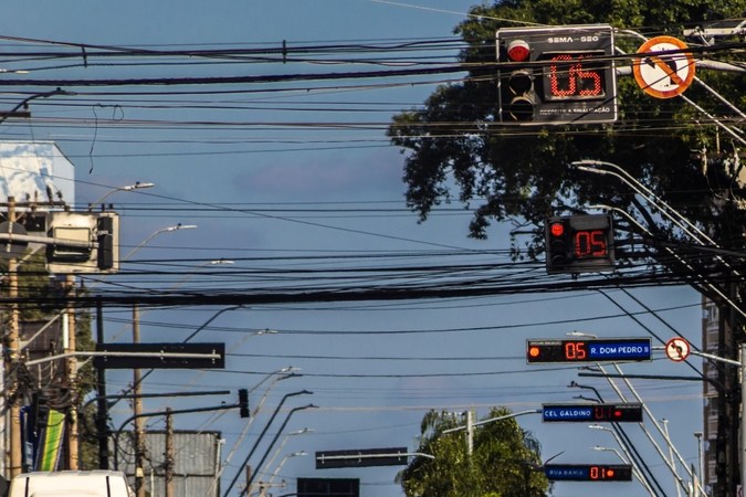 Calle con semáforos en rojo, contadores digitales y tráfico de autos y motos bajo cables.