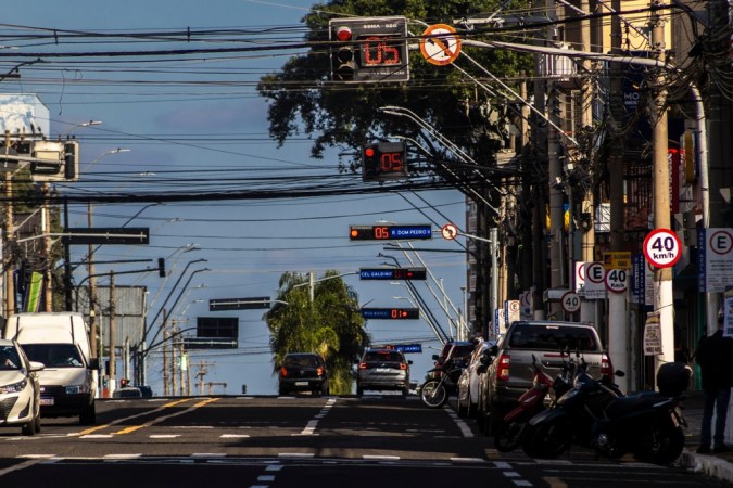 Calle con semáforos en rojo, contadores digitales y tráfico de autos y motos bajo cables.