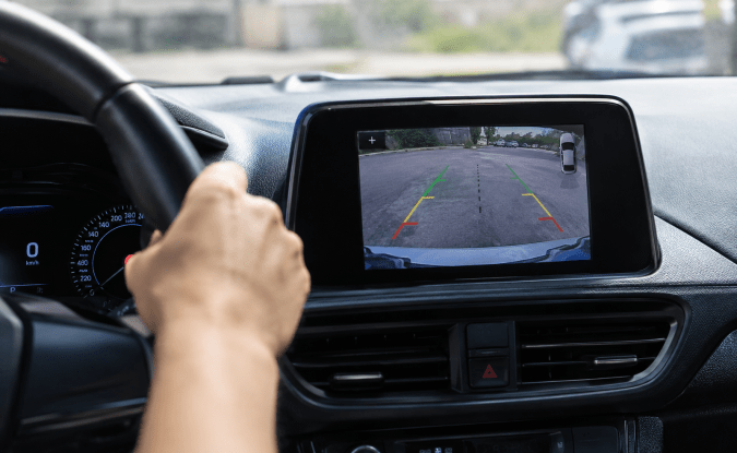 Pantalla del automóvil muestra la cámara de reversa con líneas de estacionamiento y vista trasera del vehículo.