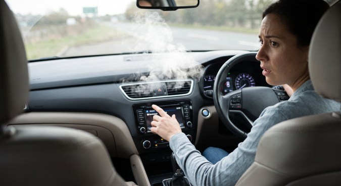 Conductora observa humo blanco del aire acondicionado mientras conduce y ajusta la pantalla multimedia del automóvil.