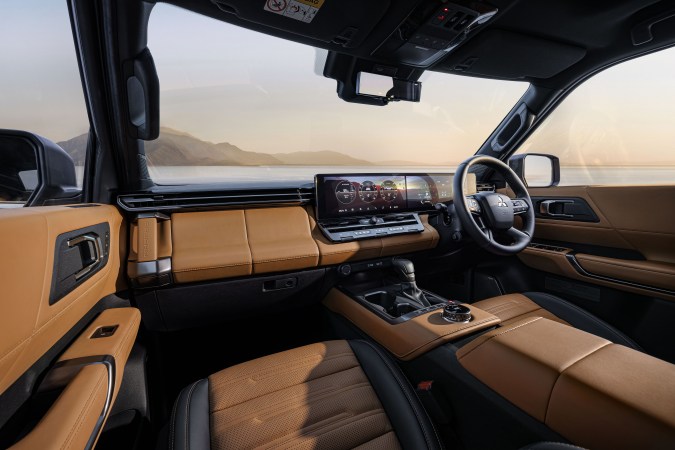 Interior delantero del Mitsubishi Pajero 2027 con tablero moderno, pantalla táctil, volante multifunción y tapicería de cuero marrón.