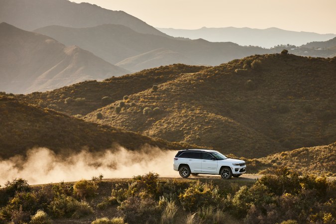 Jeep Grand Cherokee blanca circulando por un camino montañoso y levantando polvo al atardecer.