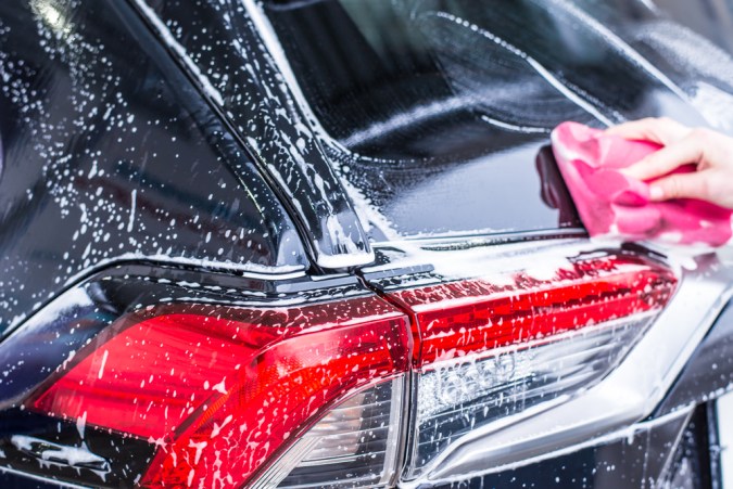Mano con paño rosa limpiando espuma de jabón en la calavera trasera de un auto negro
