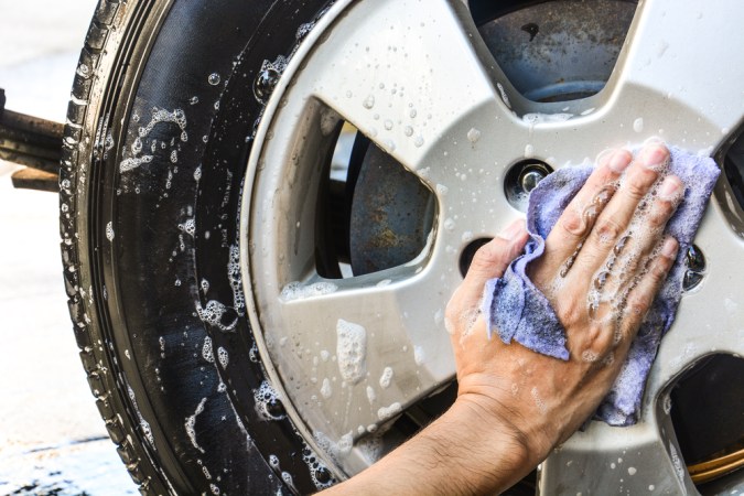 Mano limpiando rin de auto con paño de microfibra y espuma de jabón durante lavado de vehículo