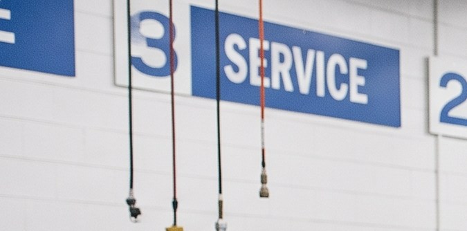 Mecánico revisando el motor de un sedán en un taller de servicio mientras explica el diagnóstico a los clientes.