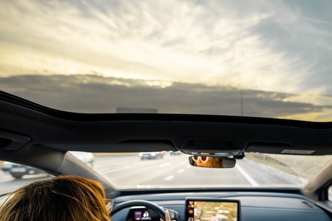 Una mujer conduce un coche con una azotea panorámica al atardecer. Vista interior desde el fondo. Coches modernos y concepto de viajes