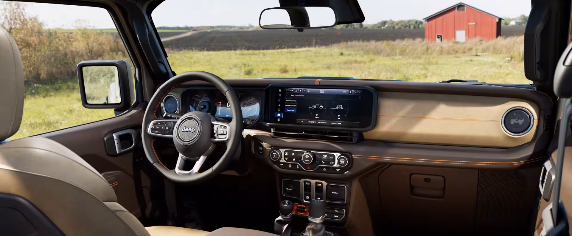 Interior del Jeep Wrangler con tablero en tonos marrón y arena, pantalla táctil multimedia y volante multifunción con costuras decorativas.