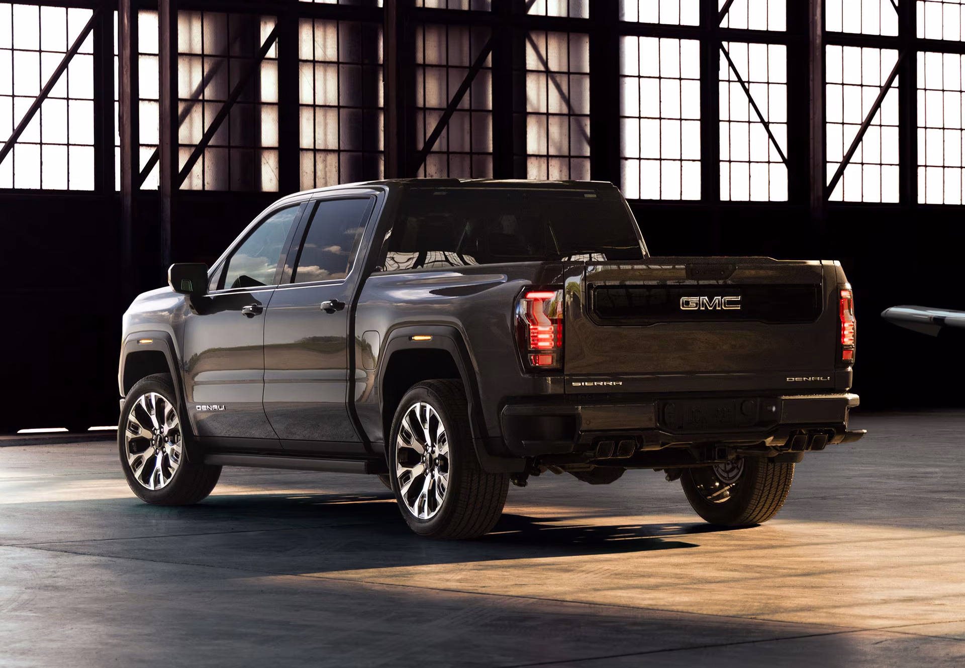 Vista trasera de la camioneta GMC Sierra 1500 Denali gris oscura estacionada en un almacén industrial con grandes ventanales.