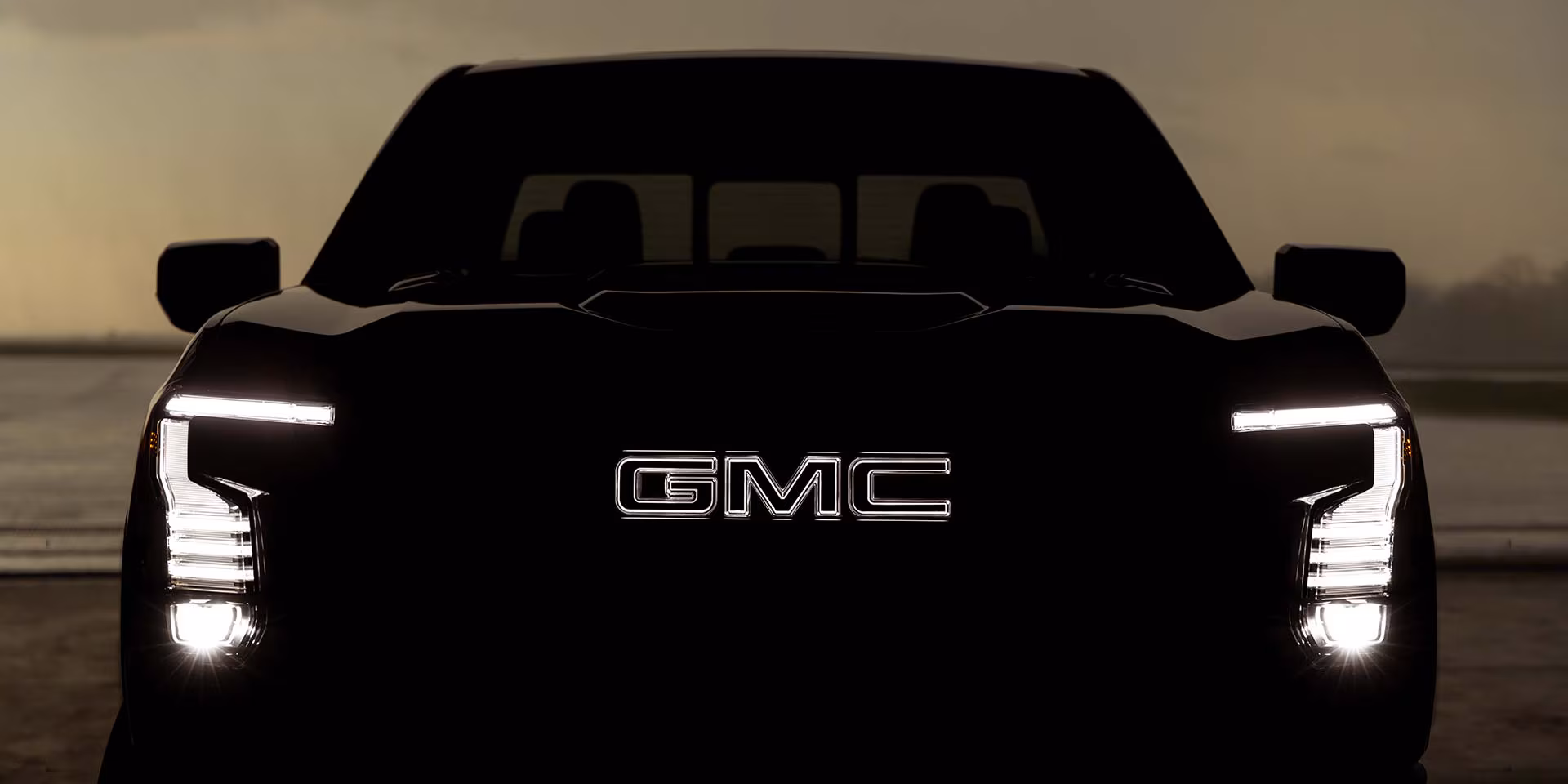 Silueta frontal oscura de la GMC Sierra 1500 destacando el logotipo central y los faros LED en forma de C iluminados.