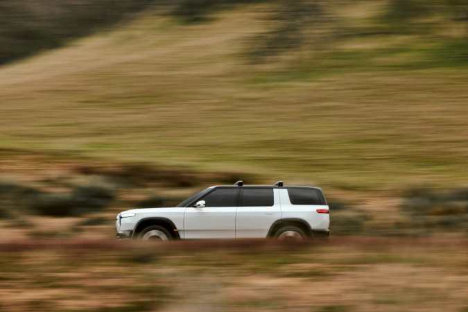 Rivian R2 blanco 2027 acelerando por camino de tierra con paisaje de colinas.