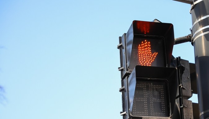 Semáforo peatonal rojo con mano iluminada, señal One Way y bandera estadounidense en ciudad.