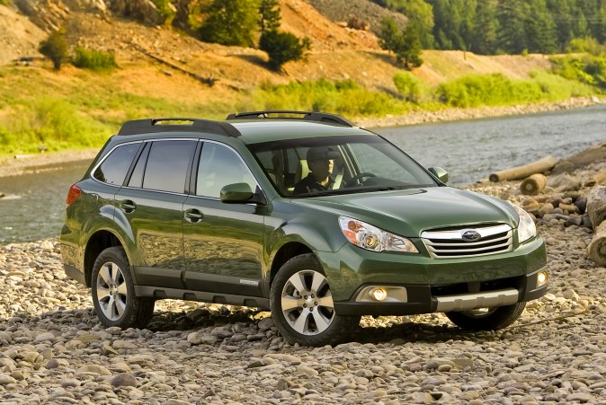 Subaru Outback 2012 verde junto a río con conductor, estilo outdoor.