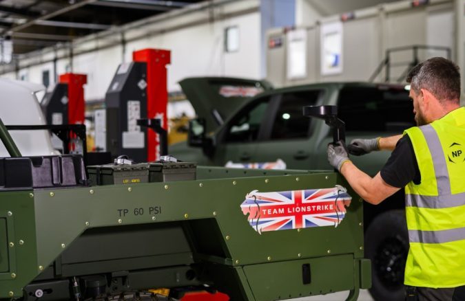 Técnico aplica calcomanía Team Lionstrike a vehículo militar verde en taller de ensamblaje.