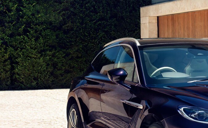 Aston Martin DBX GT púrpura metálico en entrada con arquitectura moderna