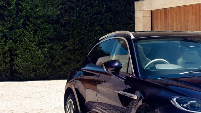 Aston Martin DBX GT púrpura metálico en entrada con arquitectura moderna