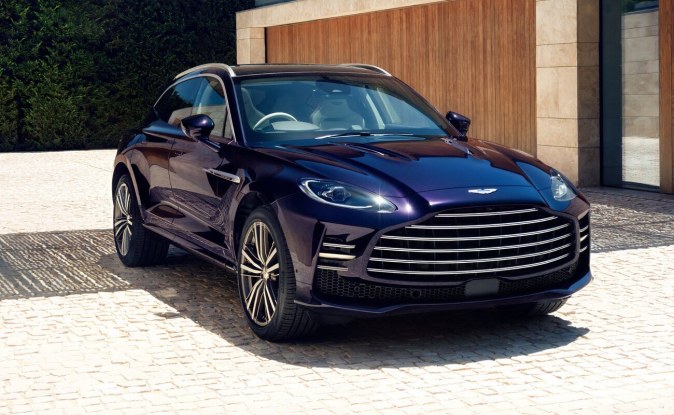 Aston Martin DBX GT púrpura metálico en entrada con arquitectura moderna