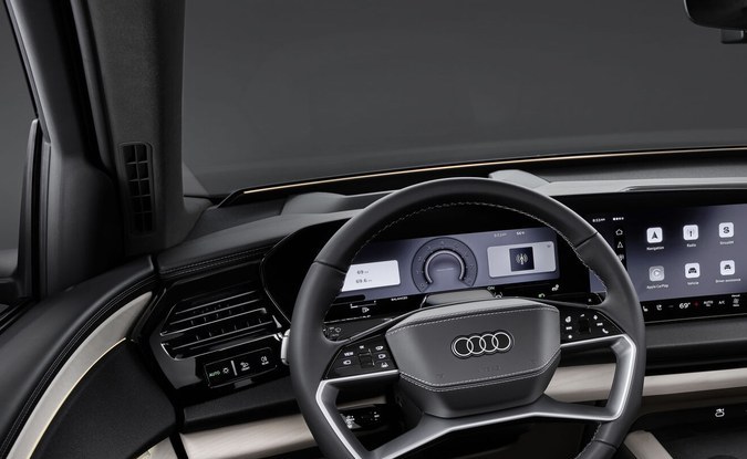 Interior del Audi Q9 con volante, pantallas digitales en el tablero y asientos de cuero gris claro.
