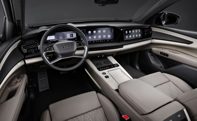Interior del Audi Q9 con volante, pantallas digitales en el tablero y asientos de cuero gris claro.