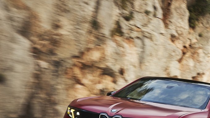 BMW iX4 M60 xDrive rojo circulando por una carretera de montaña con curvas junto a un acantilado.