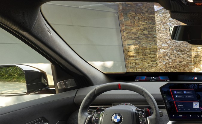 Interior del BMW iX4 con volante deportivo, pantalla central y asientos delanteros en tonos oscuros.