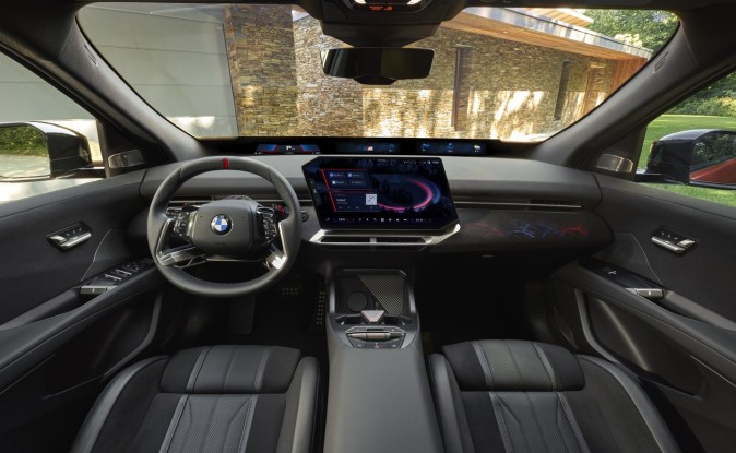 Interior del BMW iX4 con volante deportivo, pantalla central y asientos delanteros en tonos oscuros.