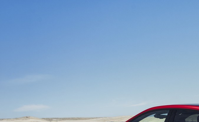 Vista trasera de tres cuartos de un BMW iX4 M60 xDrive rojo estacionado frente al mar.