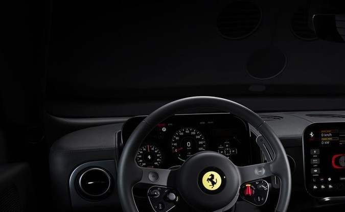 Cabina oscura del Ferrari Luce con volante de tres brazos, pantalla central y consola.