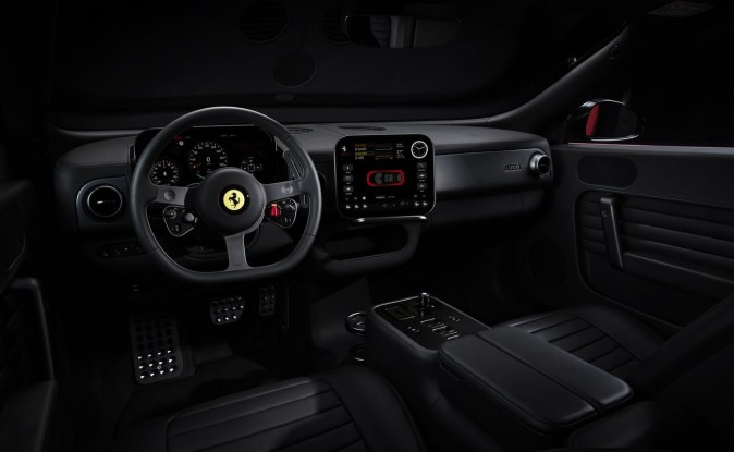 Cabina oscura del Ferrari Luce con volante de tres brazos, pantalla central y consola.