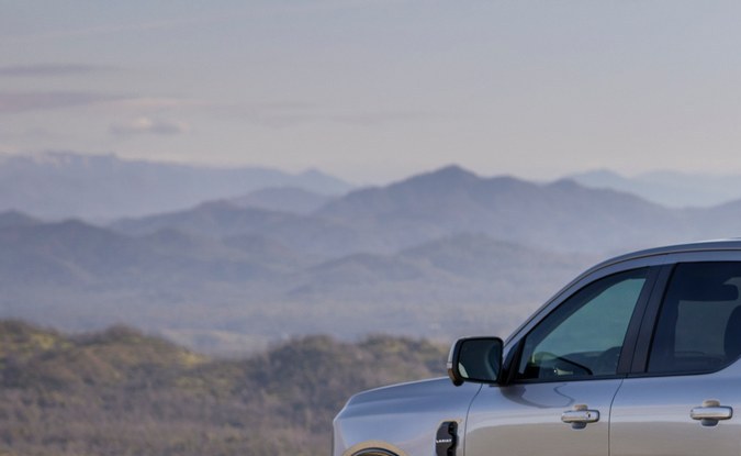 Parte trasera de una Ford Ranger plateada estacionada en un mirador de grava frente a montañas.