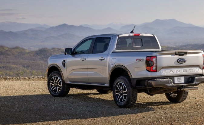 Parte trasera de una Ford Ranger plateada estacionada en un mirador de grava frente a montañas.