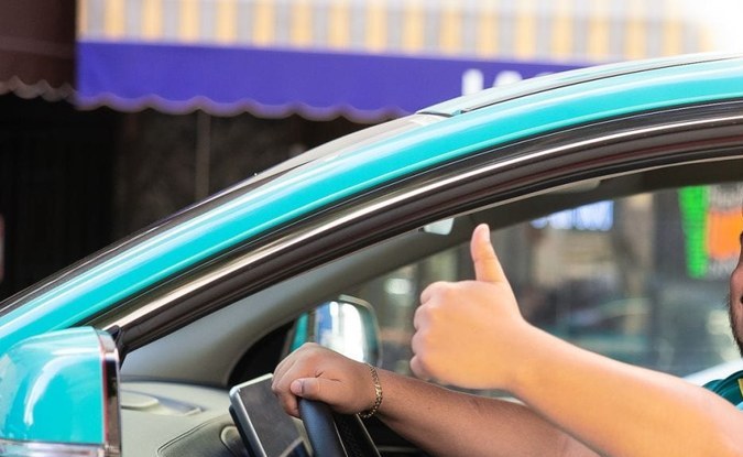 Conductor sonriente con el pulgar arriba al volante de un auto turquesa de Green SM.