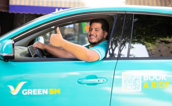 Conductor sonriente con el pulgar arriba al volante de un auto turquesa de Green SM.