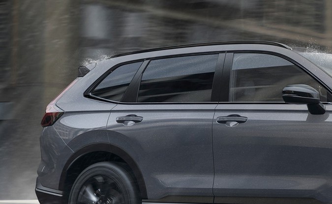Honda CR-V gris con rines negros vista de perfil mientras circula por una calle mojada.