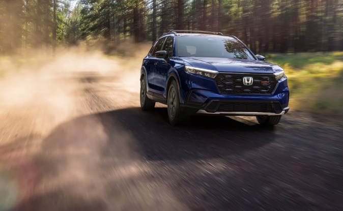 Honda CR-V TrailSport azul levantando polvo en un camino de tierra en medio de un bosque.