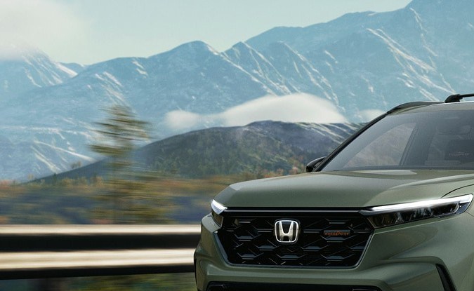 Honda CR-V TrailSport verde circulando por una carretera con montañas nevadas al fondo.