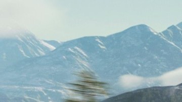 Honda CR-V TrailSport verde circulando por una carretera con montañas nevadas al fondo.