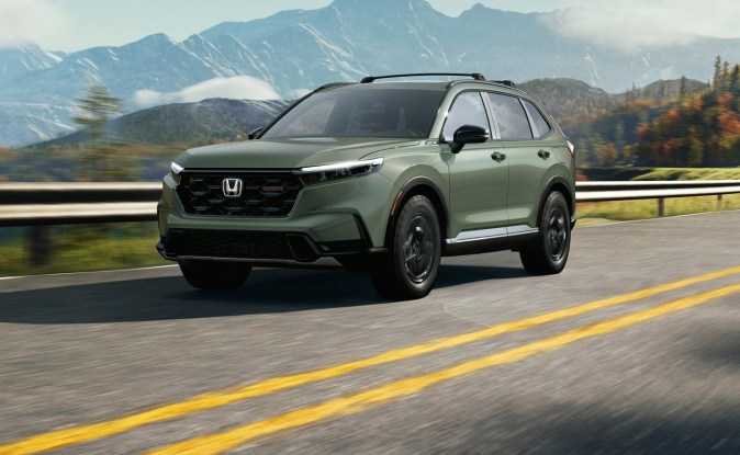 Honda CR-V TrailSport verde circulando por una carretera con montañas nevadas al fondo.