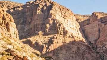 Jeep Gladiator Rubicon con llantas todoterreno grandes avanzando sobre rocas en un cañón desértico.