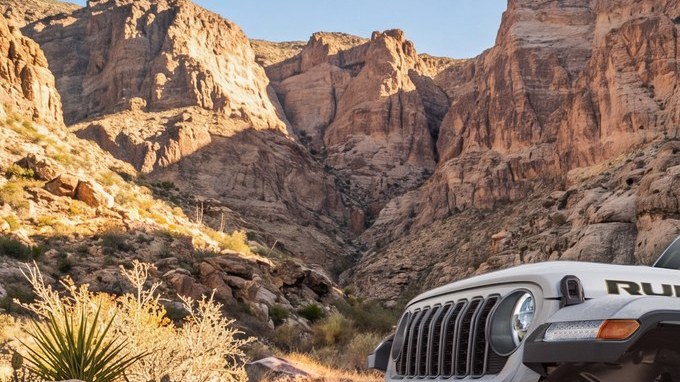 Jeep Gladiator Rubicon con llantas todoterreno grandes avanzando sobre rocas en un cañón desértico.