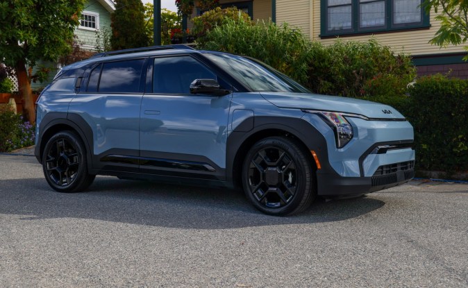 Kia EV3 2027 azul claro estacionado en una calle residencial junto a una casa con jardín
