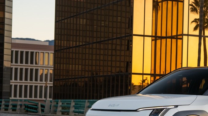 Kia EV3 2027 blanco con techo negro estacionado frente a un edificio de cristal dorado y palmeras